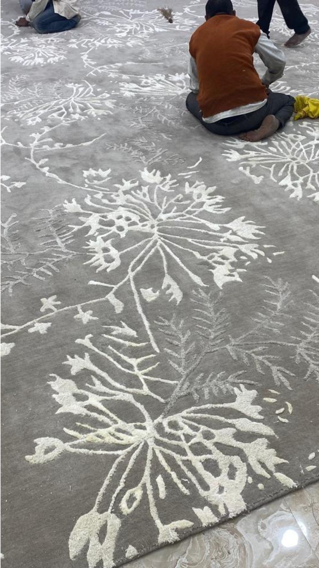 Artisan hand-tufting a large grey floral rug on the floor at MR Enterprises Panipat workshop